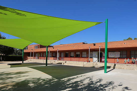 A green shade installation in a school playground, the green fabric creates a green shade on the ground.